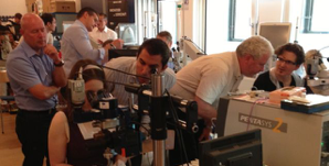 Wetlab der Sommerakademie: Teilnehmer und Referenten an einem Operationsmikroskop